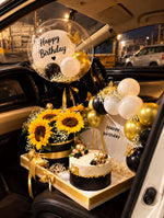Load image into Gallery viewer, Luxury sunflower birthday arrangement with black and gold ribbons, white balloons, and decorated cake.