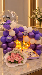 Violet Forever anniversary arrangement with purple balloons, pink roses, cake and luxury love décor