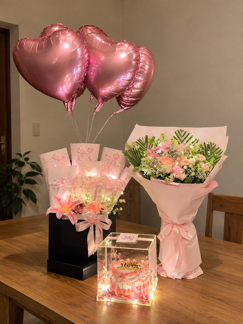 Blush Petal Symphony gift arrangement with pink flowers, heart balloons and glowing cake display