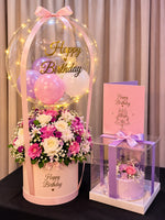 Load image into Gallery viewer, Pink birthday flower hatbox beneath a clear lighted balloon, beside a lilac floral cake in a clear ribboned box and a pink birthday card.