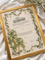 Load image into Gallery viewer, Personalised ivory Nikah certificate with sage-green floral borders, Arabic calligraphy, golden frame, and matching floral pens with green satin bows.