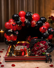 Rouge Eclipse red and black celebration setup with balloon arch, red roses, chocolate cake and fairy lights
