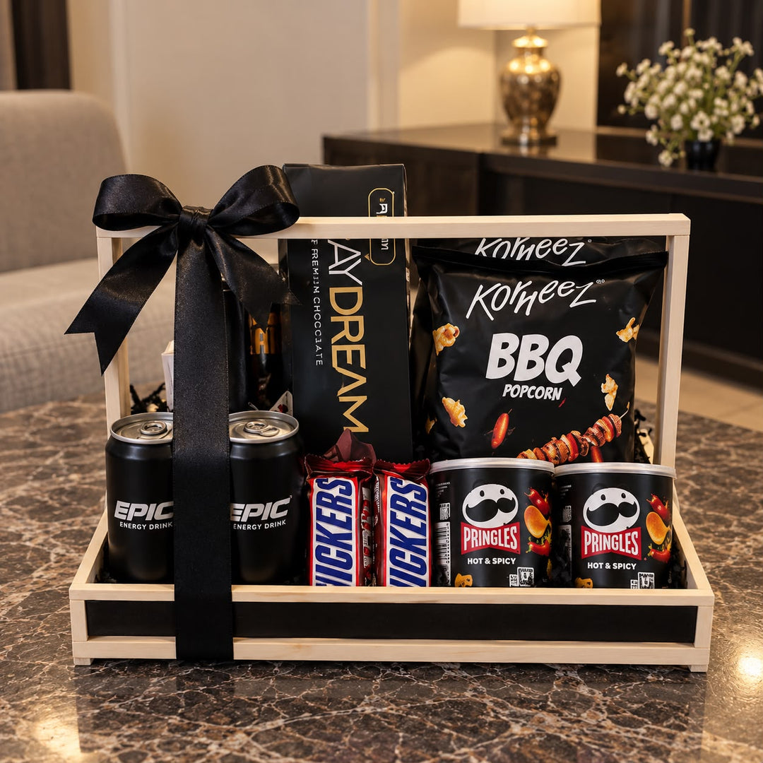 Wooden snack gift hamper with black ribbon, chocolates, popcorn, chips, and drinks arranged in a premium gift crate.