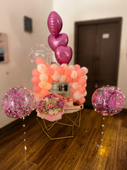 Pink balloon arrangement with floral bouquet and decorated cake
