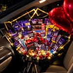 Load image into Gallery viewer, Large chocolate bouquet in black and gold wrapping with assorted chocolate bars, a mini teddy, red roses, fairy lights, and red heart balloons.