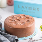 Load image into Gallery viewer, Chocolate Petal Cake with smooth chocolate frosting and petal-shaped decorations on top, displayed on a blue cake board