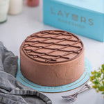Load image into Gallery viewer, Chocolate Lattice Cake with smooth chocolate frosting and a crisscross chocolate pattern on top, displayed on a blue cake board
