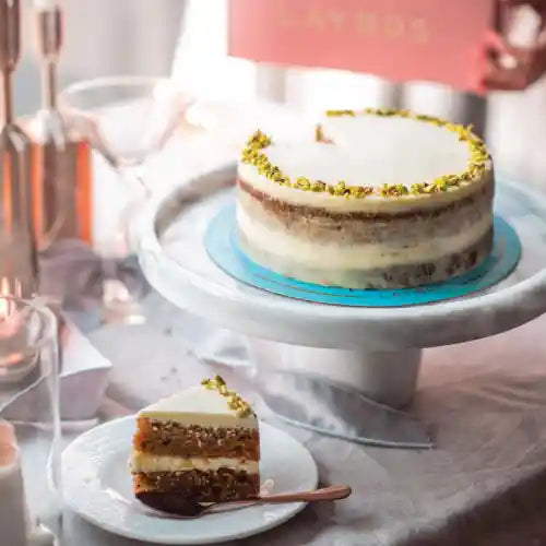 Layered nut cake with white cream frosting, chopped nut decoration and a slice showing its layered filling.