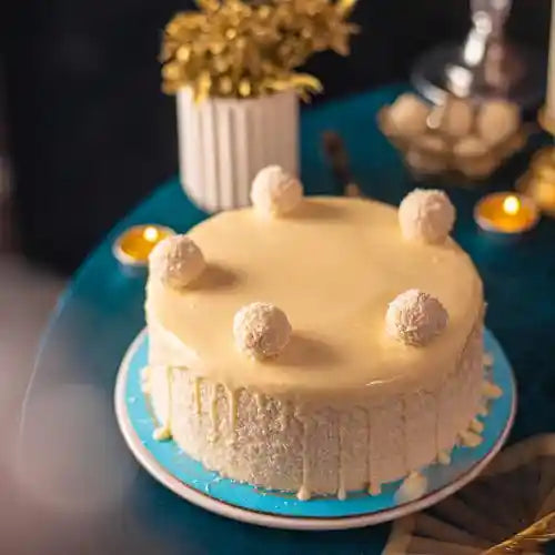 Ivory Raffaello-style cake decorated with coconut-coated truffles on a turquoise cake stand.