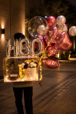 Load image into Gallery viewer, Decorative setup with HBD balloons, custom cakes and flowers on a street at night.