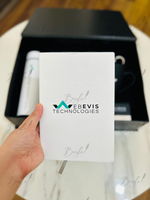 Load image into Gallery viewer, A hand holds a white branded card or booklet in front of an open black gift box containing a white cylindrical item, on a light marble tabletop with a wooden floor in the background. The card shows the WEBEVIS TECHNOLOGIES logo.