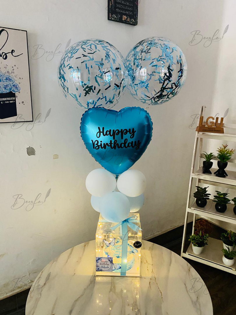 Blue birthday balloon arrangement with confetti balloons and transparent cake gift box
