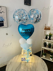 Blue birthday balloon arrangement with confetti balloons and transparent cake gift box