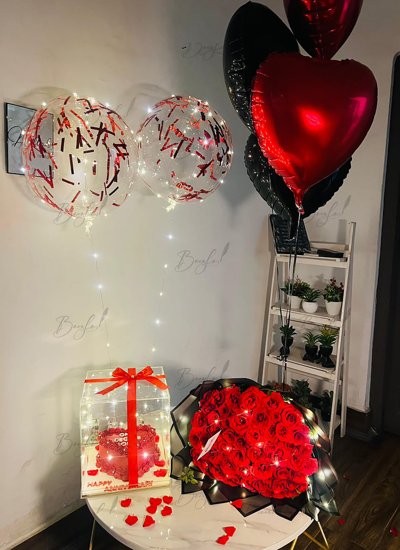 Premium celebration gift featuring red roses, transparent cake box, balloon decoration, and fairy lights