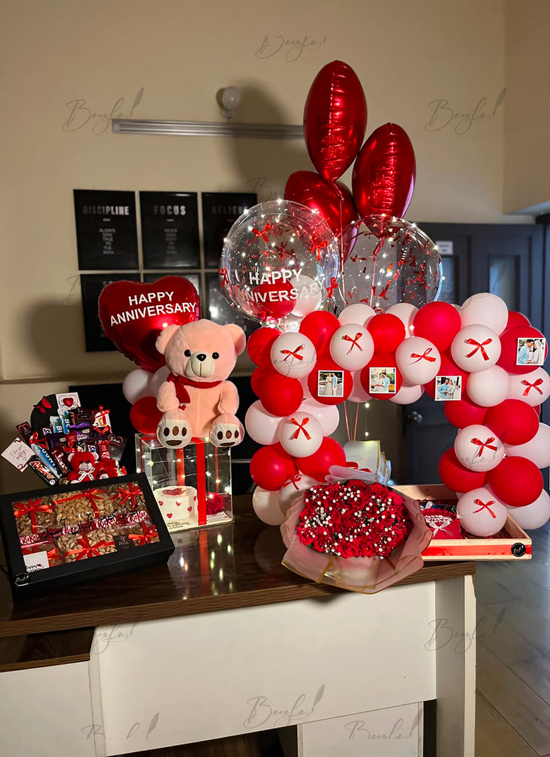 Customized anniversary surprise with personalized photo balloons, red and white balloon arch, teddy bear, chocolates, and fresh flower bouquet