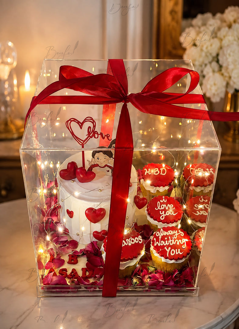 Signature Love Box with romantic cake, decorated cupcakes, fairy lights, heart accents, and red ribbon in a luxury acrylic gift box.