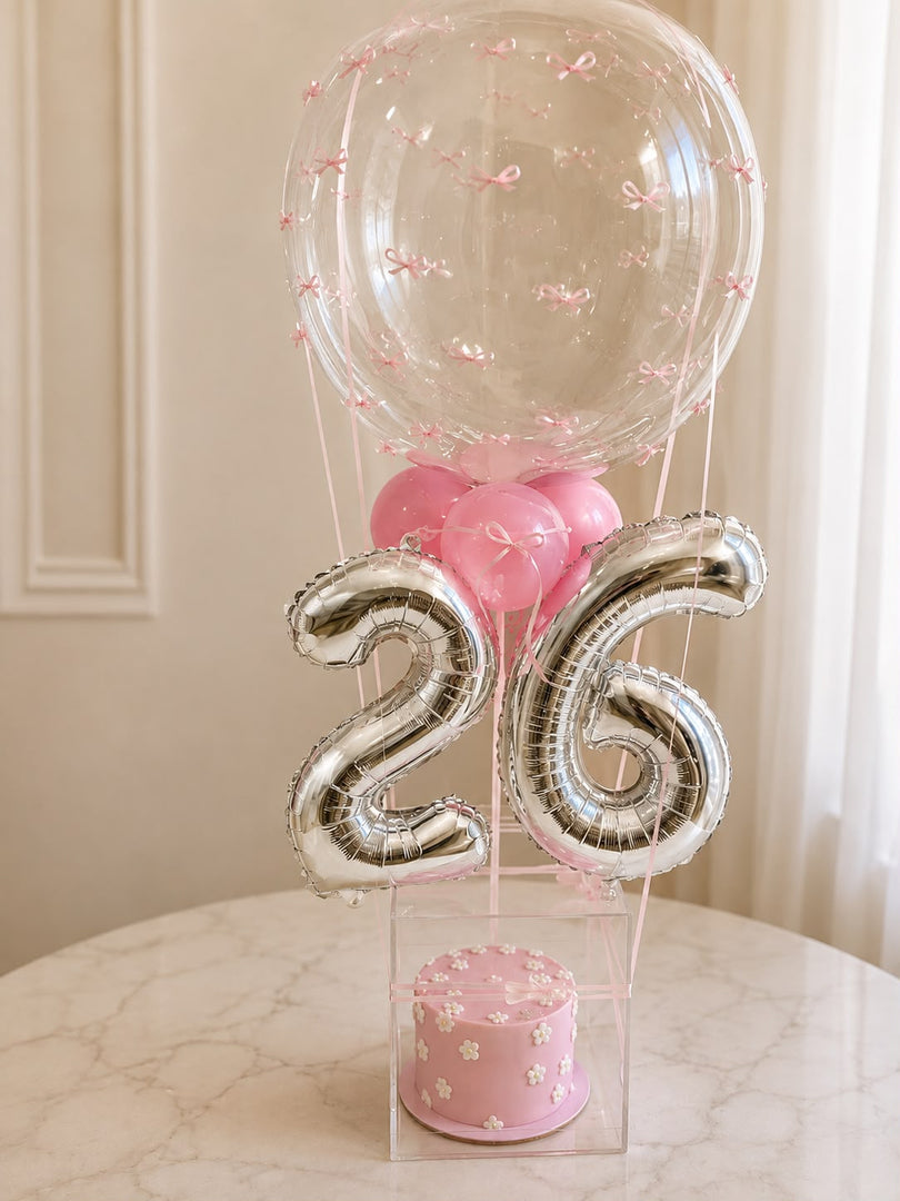 Petal Grace pink birthday cake with floral details, silver number balloons, pink balloons, and clear acrylic display