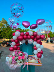 Magenta and white balloon arch with pink flower bouquet, birthday cake, heart balloons, and gift tray
