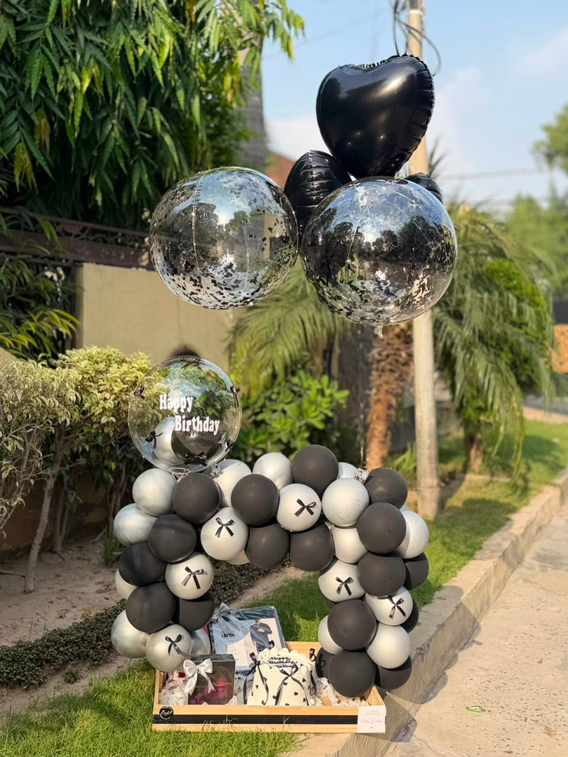 Noir Birthday Charm with black and silver balloon arch and gift box