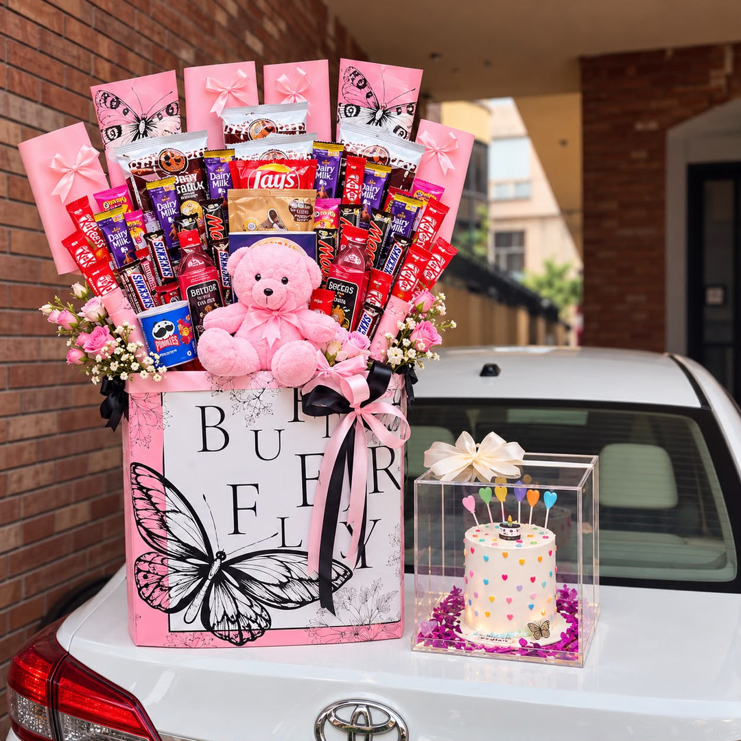 Pink butterfly chocolate and snack hamper with a teddy bear, displayed beside a boxed celebration cake and pink-wrapped red roses.