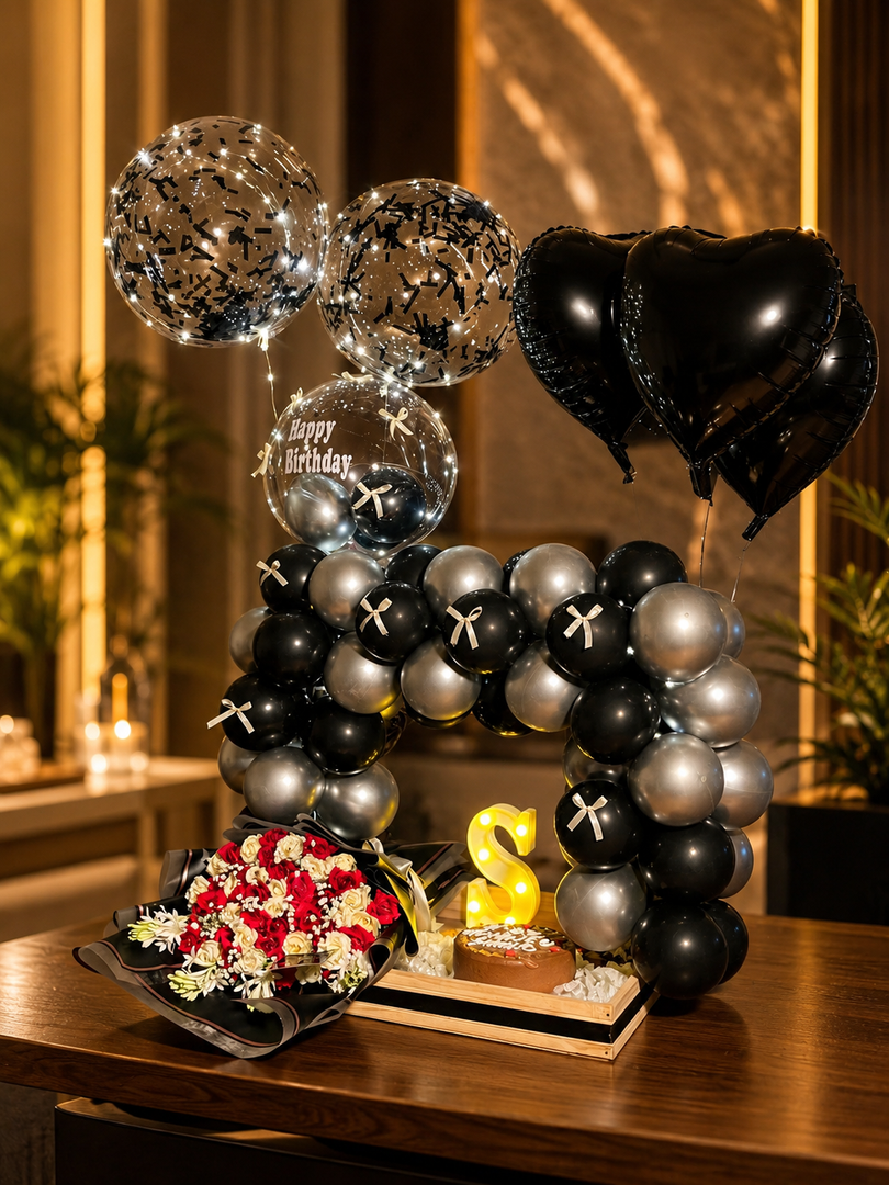 Luxury black and silver birthday setup with balloon arch, heart balloons, flowers, cake, and LED lights