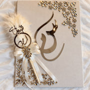 Luxury beige calligraphy keepsake with gold-tone Arabic lettering, crystal floral embellishments, and an ivory satin ribbon.