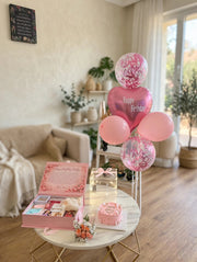 Pink birthday gift arrangement with confetti balloons, beauty gift box, pink cake and floral bouquet
