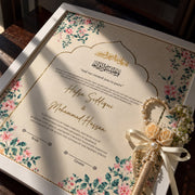 Personalised ivory Nikah certificate with pink flowers, green foliage, Arabic calligraphy, gold borders, and a matching rose-decorated Nikah pen.