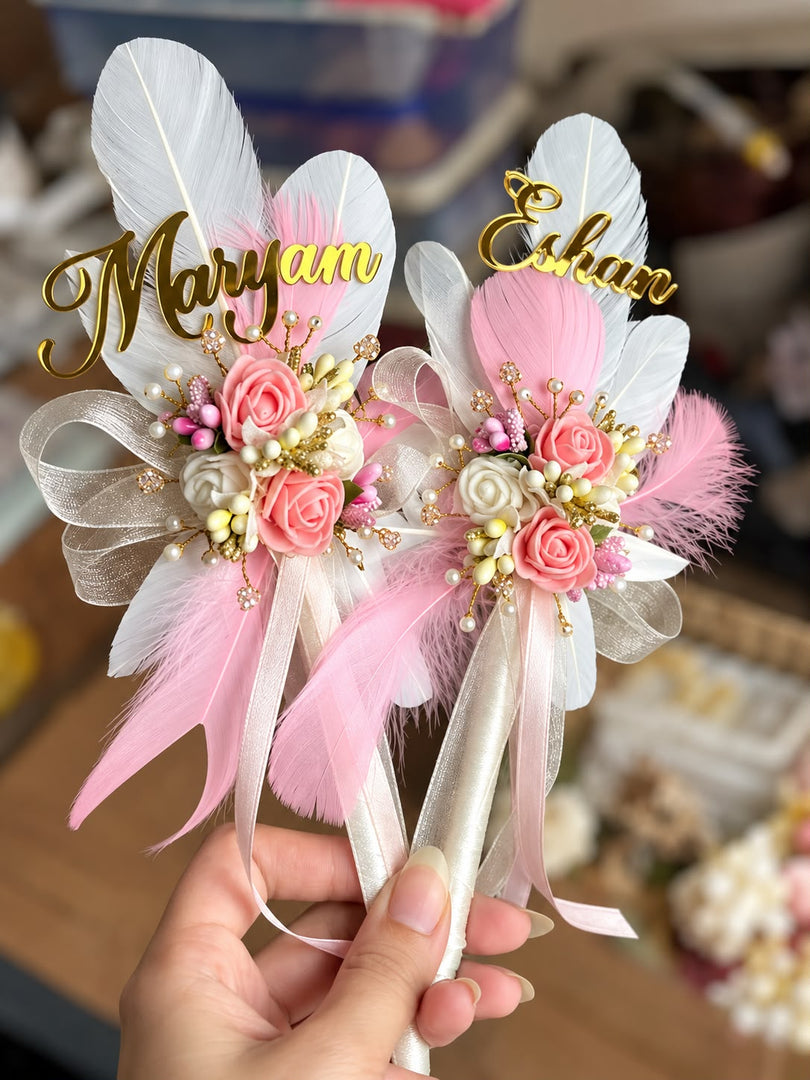Personalised Nikah pens with pink and white feathers, rose flowers, pearl accents, satin ribbons, and gold name lettering.