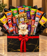 Load image into Gallery viewer, Choco Crunch Hamper with assorted chocolates, snack packets, a teddy bear and a red ribbon on a black gift box.