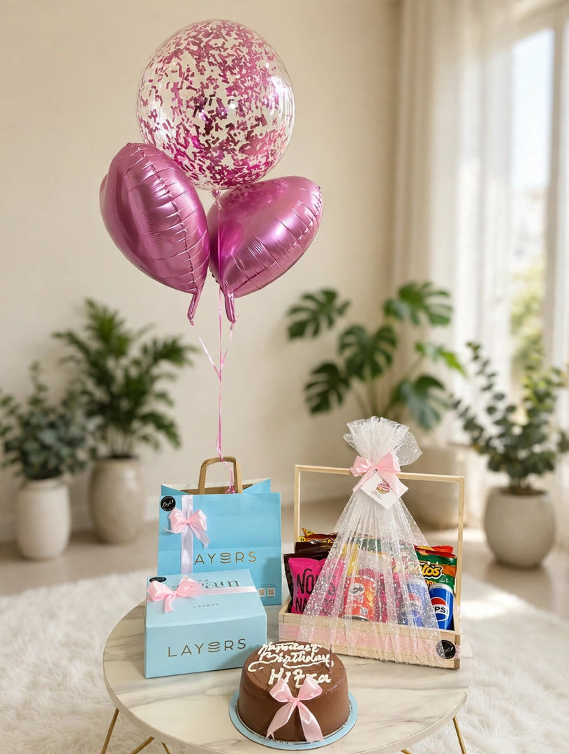 Birthday gift pack with a bow-decorated cake, wrapped wooden snack hamper, blue gift packaging, and three pink-themed balloons.