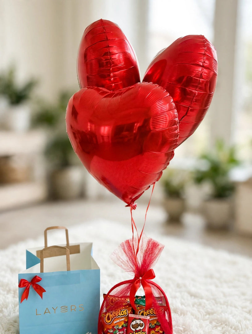 Three shiny red heart-shaped foil balloons with red ribbons tied to a birthday snack hamper.