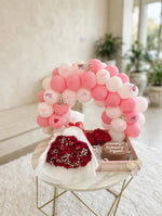 Load image into Gallery viewer, Red roses in white wrapping beside a birthday cake with chocolate-coloured frosting, displayed beneath pink and white balloons.