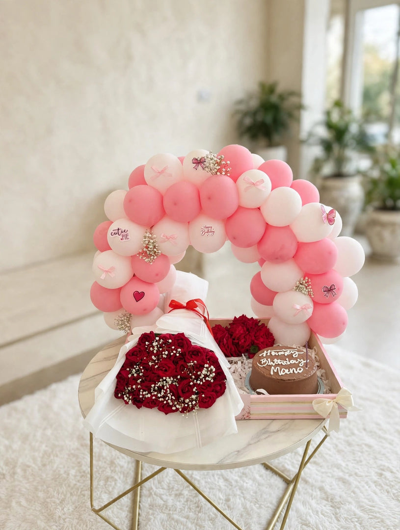 Red roses in white wrapping beside a birthday cake with chocolate-coloured frosting, displayed beneath pink and white balloons.