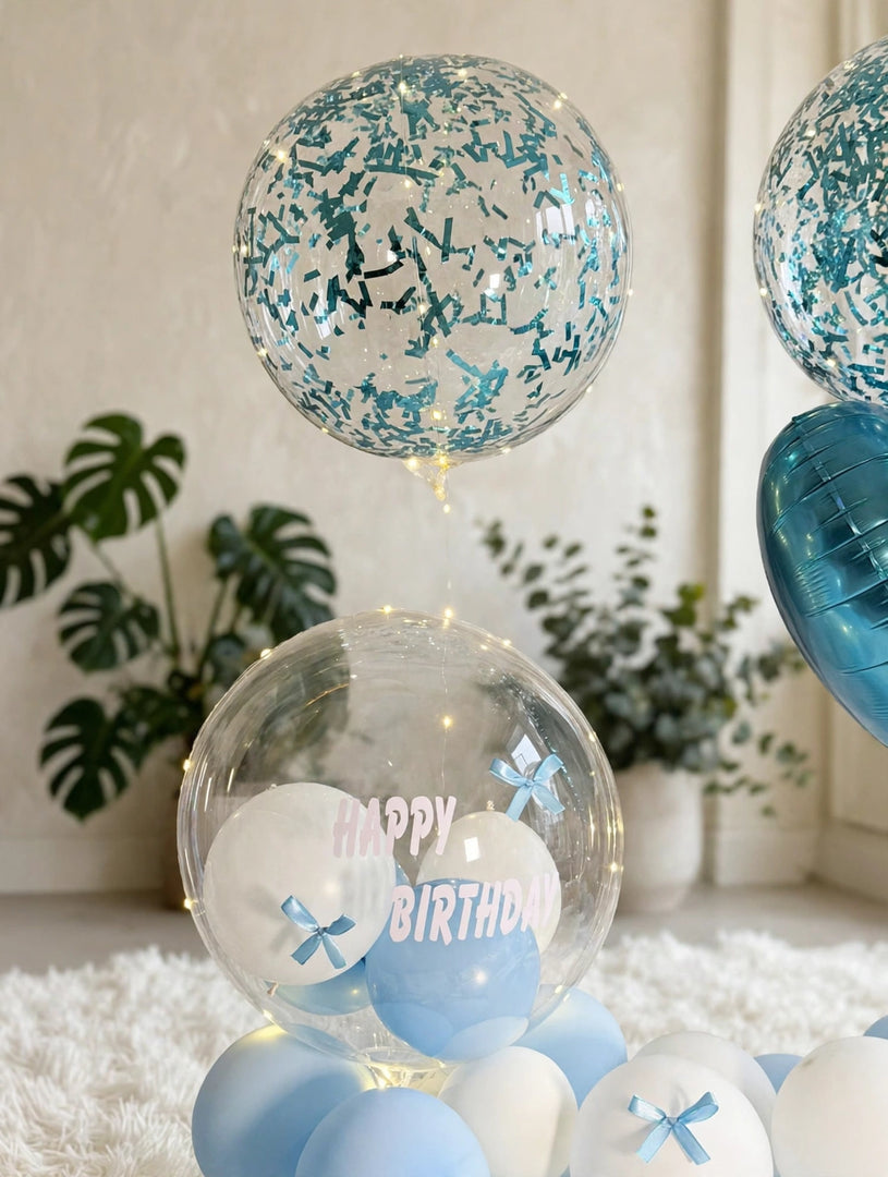 Clear Happy Birthday balloon filled with small blue and white balloons, decorated with blue bows and warm fairy lights.