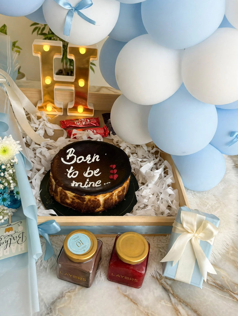 Round birthday cake with a dark topping, white piped lettering, and patterned sides, nestled in a wooden gift tray.
