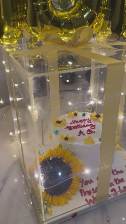 Premium birthday surprise featuring a glowing acrylic gift box, cake, gold foil balloons, LED fairy lights, and customized birthday balloon arrangement.